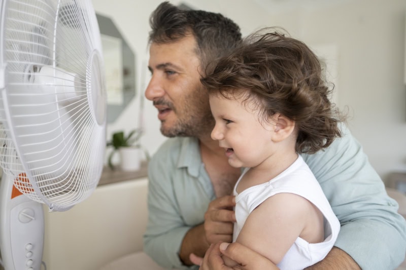 father and toddler sitting in front of a fan together.