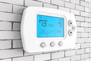 Thermostat Settings: On vs. Auto. Photo of a digital thermostat mounted on a wall with a blue light.